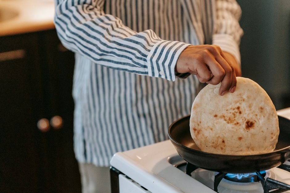 Personne en chemise rayée tenant un pain pita dans une poêle sur une cuisinière.