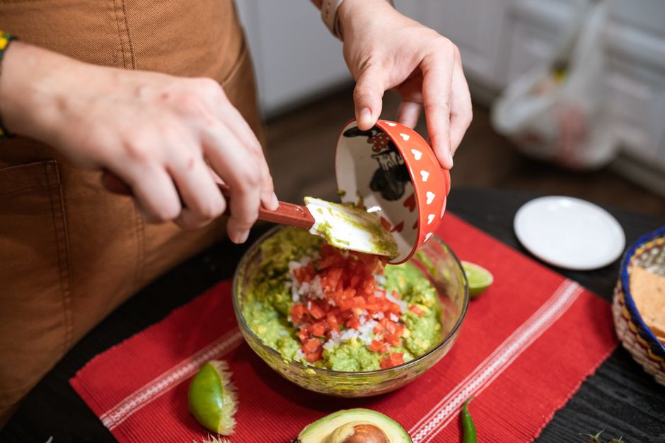 Préparation d'un guacamole avec des tomates et des oignons dans un bol en verre sur une table en bois.