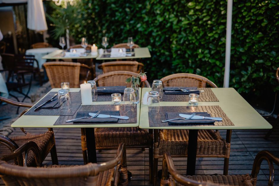 Tables dressées pour un apéro en extérieur, avec vaisselle, serviettes et décorations sur une terrasse verdoyante.