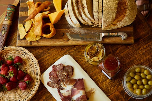 Planche apéritive avec pains, fromages, charcuterie, tapenade, olives et fraises sur une table en bois.