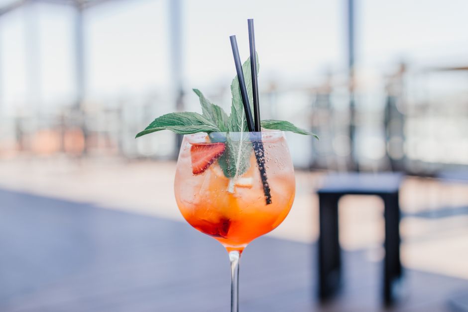 Verre de spritz maison garni de fraises et de menthe, avec des pailles, sur une terrasse ensoleillée.