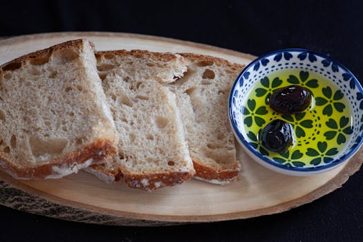 Tranches de pain sans pétrissage accompagnées d'une assiette d'huile d'olive et d'olives noires.