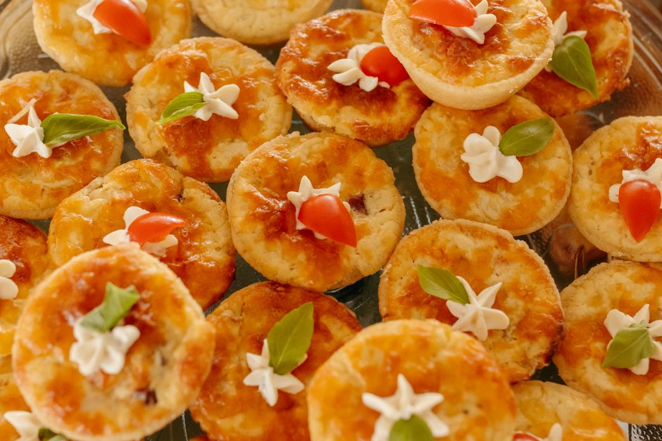 Plateau de mini quiches sans pâte garnies de jambon, légumes et saumon, décorées de tomates cerises et de basilic.