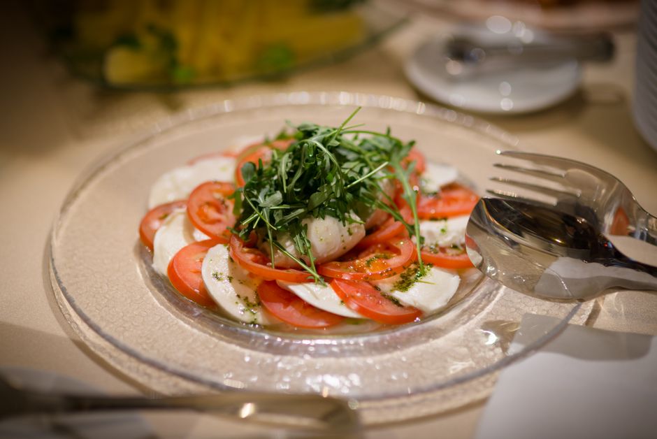 Assiette de brochettes tomate, mozzarella et basilic, garnie de jeunes pousses sur un fond clair.
