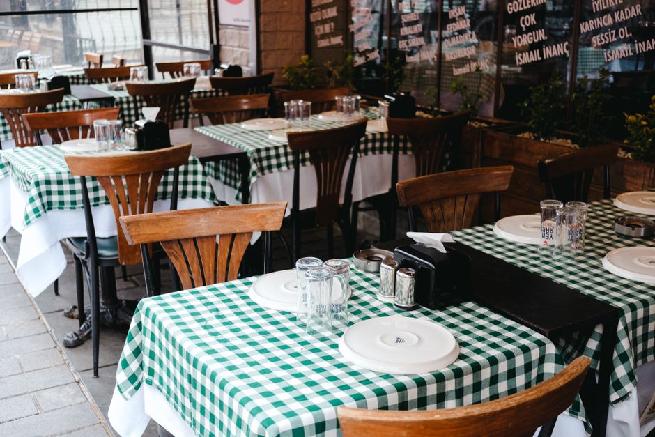 Tables en bois avec nappes à carreaux verts et blancs, prêtes pour un apéritif en extérieur. Vaisselle et verres disposés.