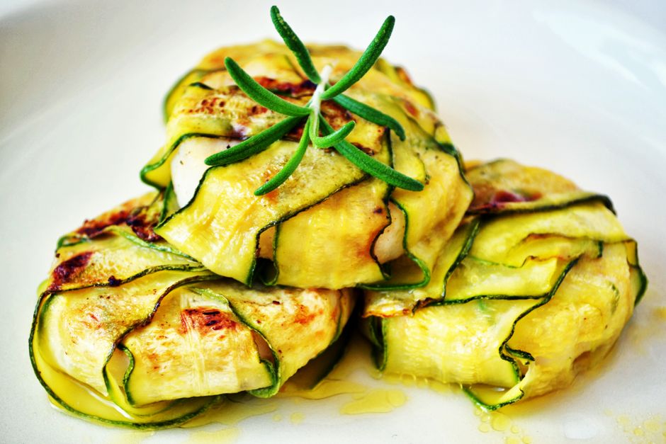 Bouchées de courgette enroulées autour de fromage de chèvre, garnies d'une herbe verte sur une assiette blanche.
