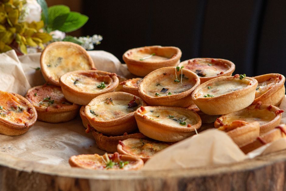 Assortiment de mini quiches sans pâte garnies de jambon, légumes et saumon sur un plateau en bois.