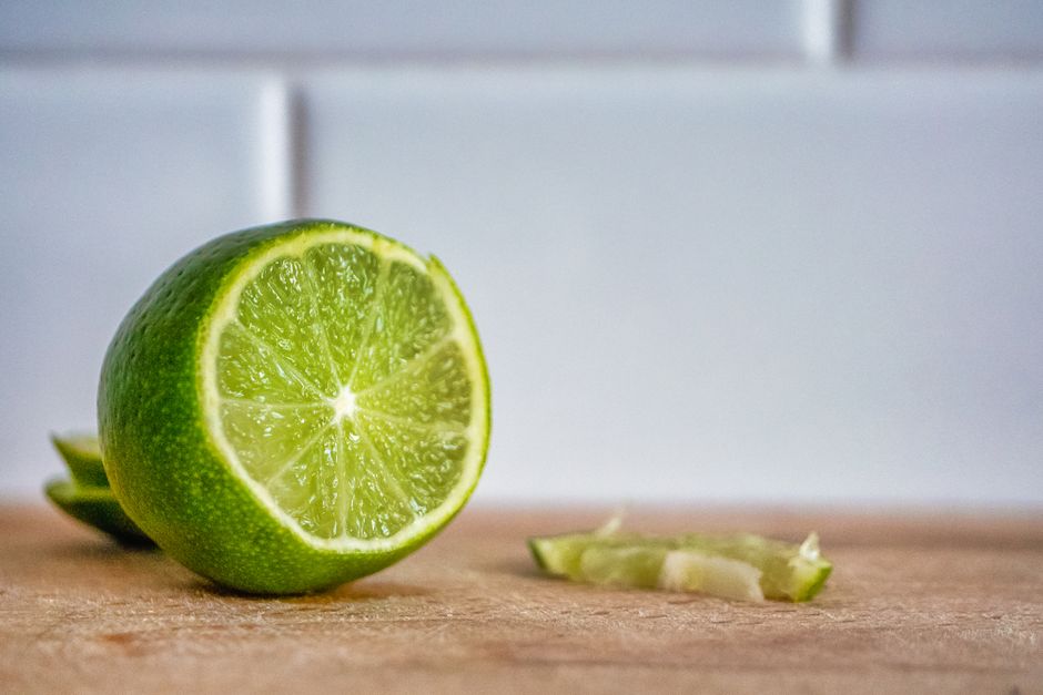 Un citron vert coupé sur une planche en bois, avec une tranche à côté, prêt pour un cocktail sans alcool.