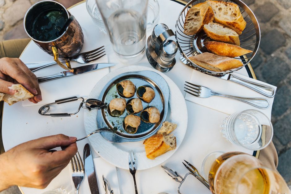 Assiette avec escargots, morceaux de pain et couverts sur une table, ambiance apéritif convivial en extérieur.