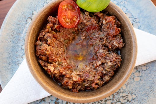 Bol de tapenade maison avec tomates cerises et basilic, servi sur une assiette décorative.