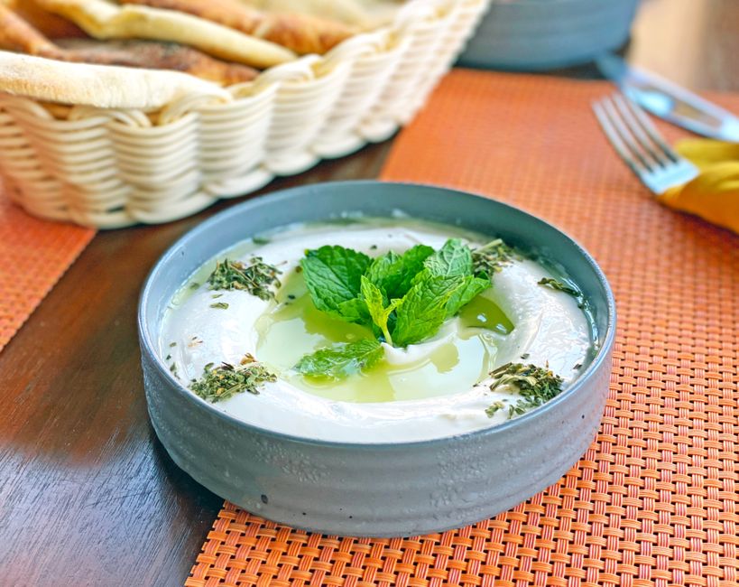 Tzatziki maison dans un bol gris, garni de menthe et d'huile d'olive, avec du pain pita en arrière-plan.