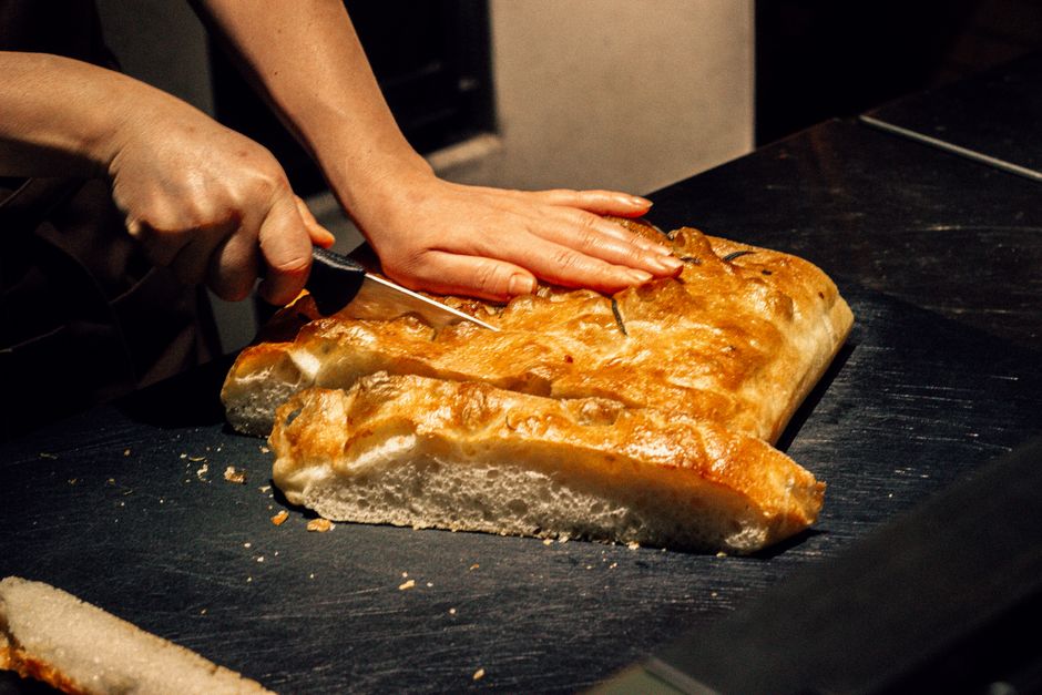 Main coupant une focaccia dorée et moelleuse sur une surface en bois, avec une texture aérée.