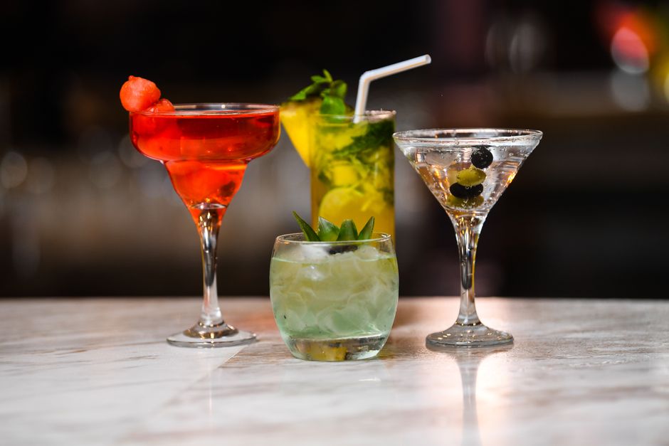Quatre cocktails colorés sans alcool sur une table en marbre, garnis de fruits et herbes fraîches.