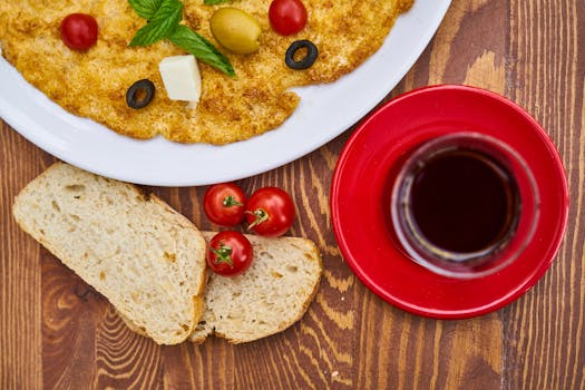 Assiette de galette dorée avec olives, tomates cerises, pain et verre de boisson sur une table en bois.