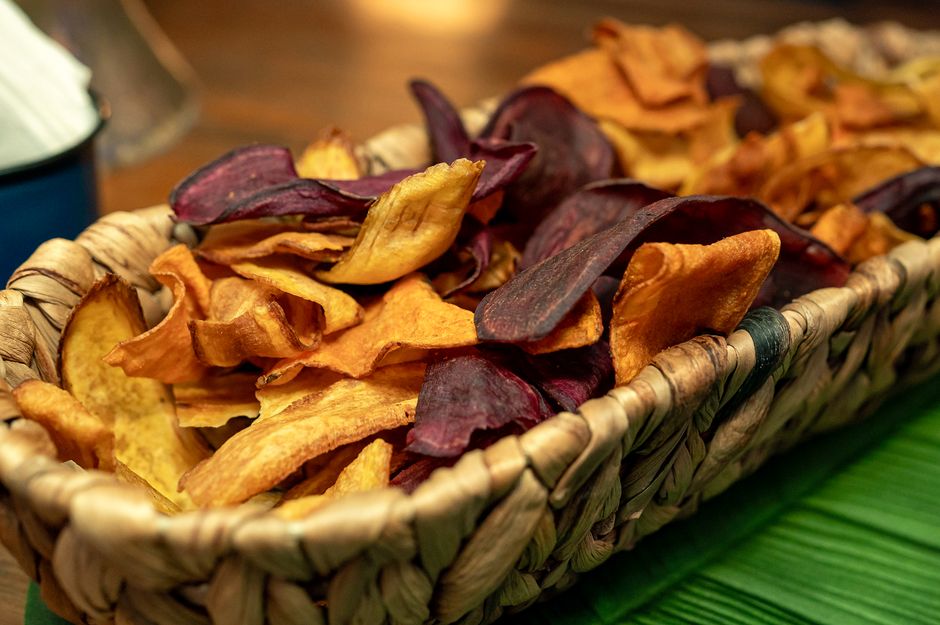 Chips de légumes au four dans un panier en osier, comprenant des tranches de betterave et de patate douce.