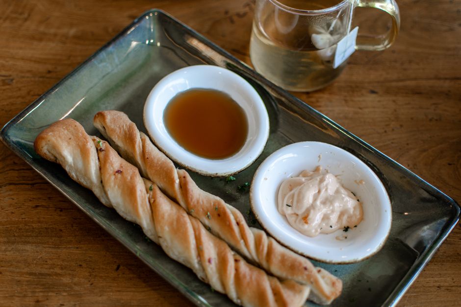 Assiette de gressins croustillants avec sauces, accompagnée d'une tasse de thé sur une table en bois.