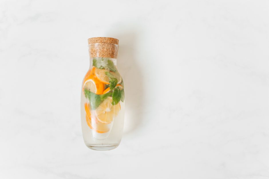 Bouteille en verre avec eau aromatisée au citron, concombre et menthe sur fond blanc.