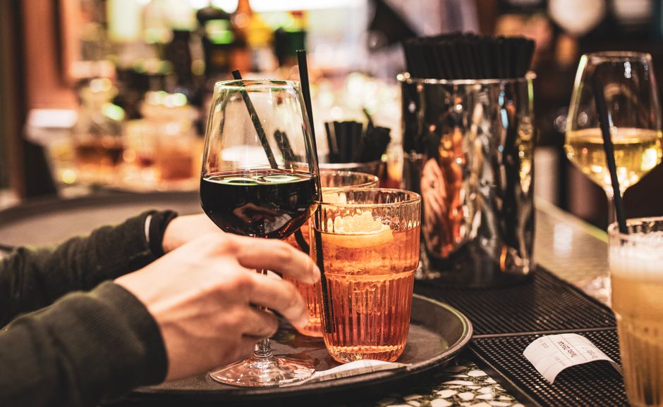 Deux verres de spritz sur un plateau, l'un avec une tranche d'orange, l'autre avec du vin rouge. Ambiance de bar.