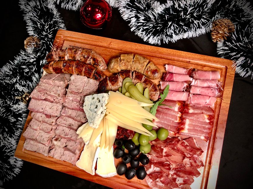 Planche apéro équilibrée avec charcuterie, fromages, olives et fruits, décorée de guirlandes festives.