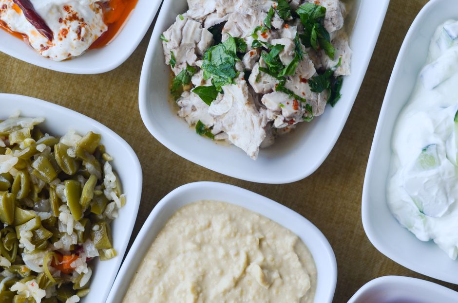 Assortiment de plats méditerranéens incluant tzatziki, poulet aux herbes, houmous et légumes marinés.