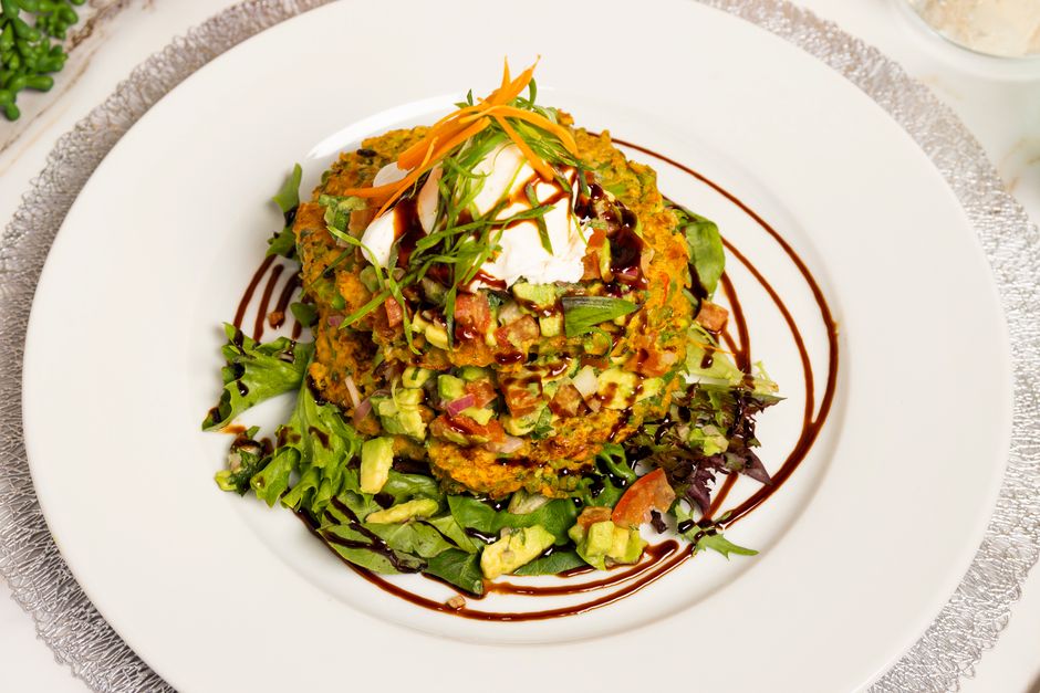 Bouchées de courgette et chèvre servies sur un lit de salade, garnies de sauce et de légumes frais.