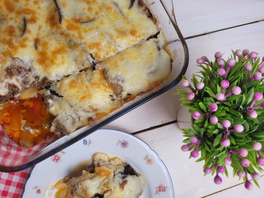 Plat de caviar d'aubergine au four, gratiné avec du fromage, servi dans un plat en verre, décoré d'une plante.