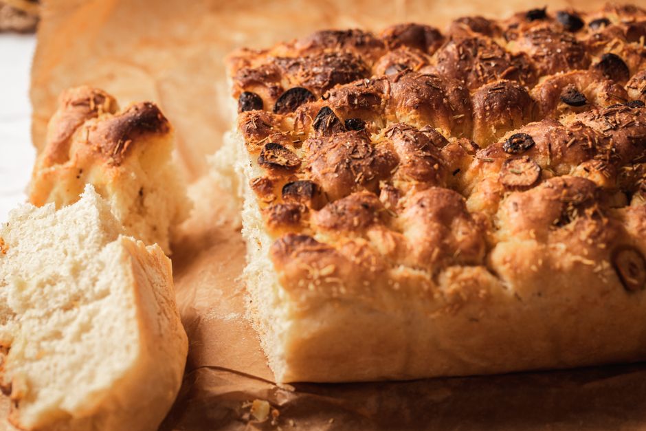 Focaccia maison dorée et moelleuse avec croûte croustillante, accompagnée d'un morceau coupé.