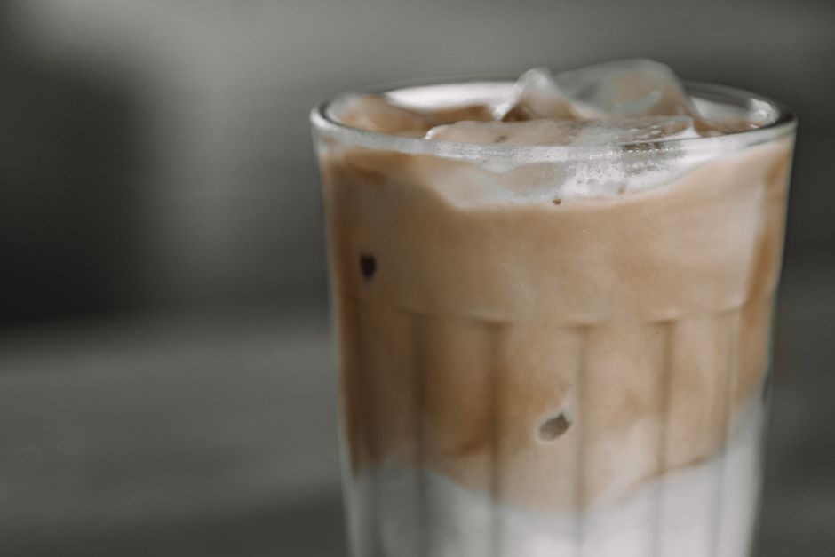 Verre de café glacé crémeux avec des glaçons, sur fond flou, évoquant une boisson rafraîchissante.