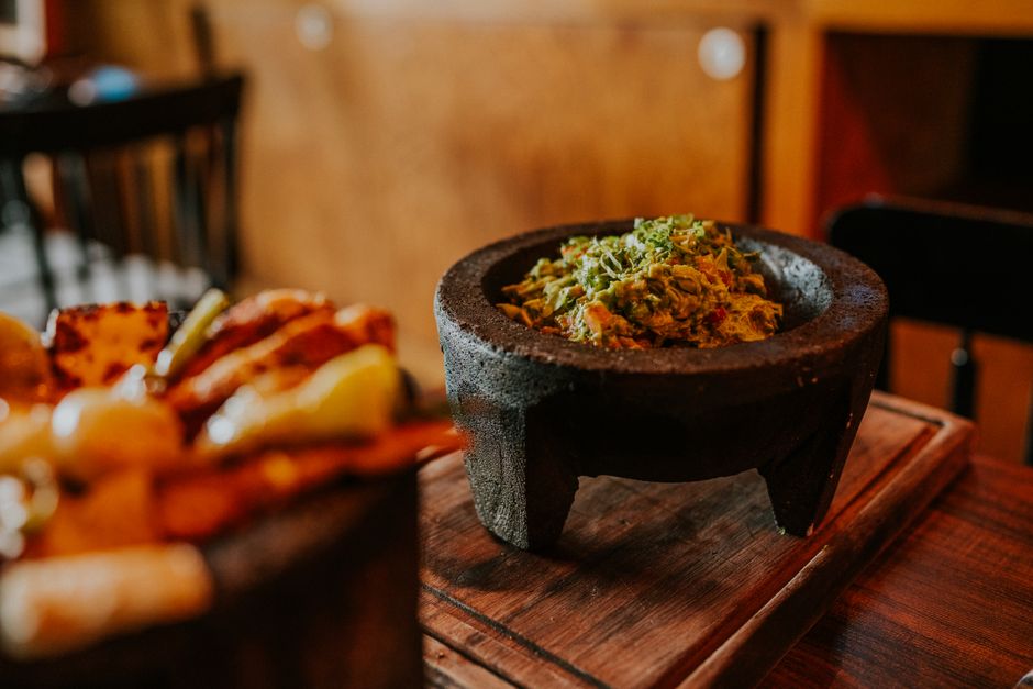 Bol en pierre rempli de guacamole bien assaisonné, avec des herbes fraîches, sur une planche en bois.