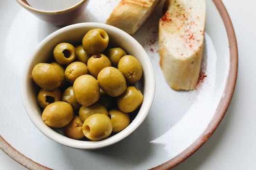 Bol d'olives vertes accompagné de tranches de pain sur une assiette, parfait pour un apéro maison.