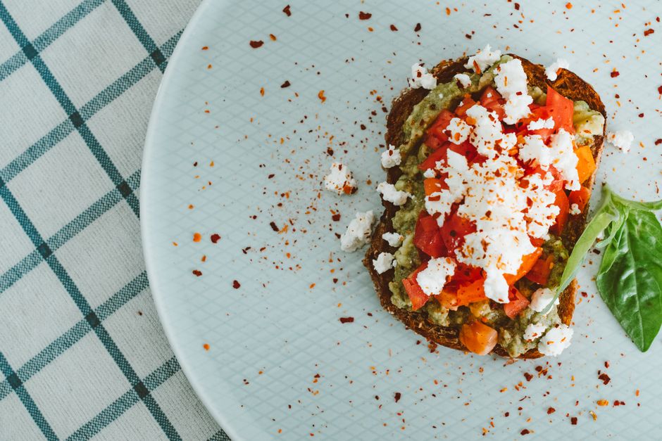 Tartine de pain complet garnie de légumes colorés, feta émiettée et épices sur une assiette.
