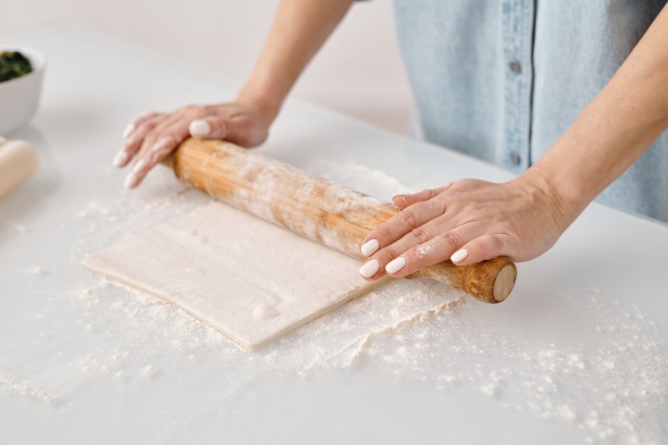 Femme roule de la pâte feuilletée sur un plan de travail fariné pour préparer des feuilletés apéritifs.