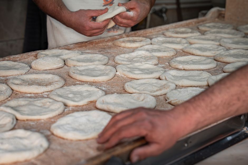 Pains pita en préparation sur une surface farinée, avec des mains façonnant la pâte.