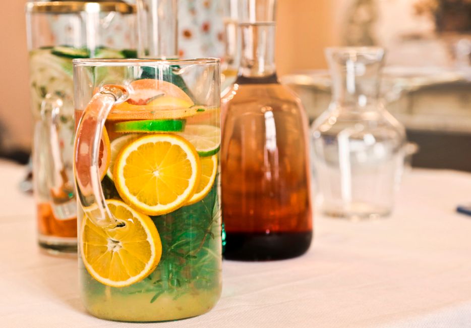 Carafe d'eau aromatisée avec tranches de citron, concombre et feuilles de menthe sur une table.