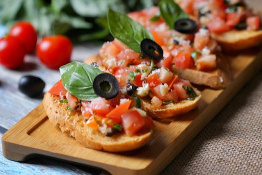 Tranches de pain garnies de tomates, olives noires et basilic sur une planche en bois, avec des tomates cerises en arrière-pl