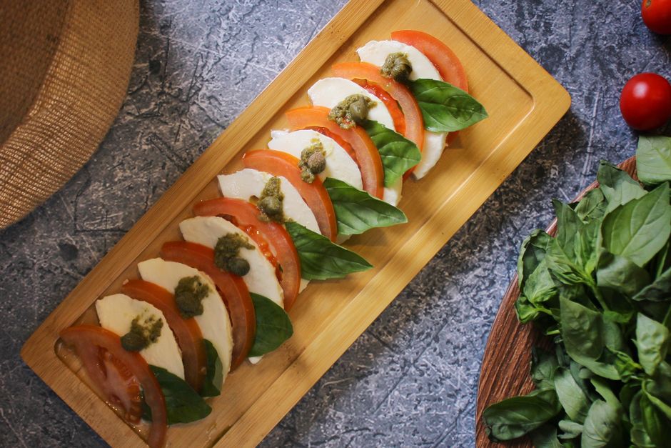 Brochettes de tomates, mozzarella et basilic sur une planche en bois, accompagnées de pesto.