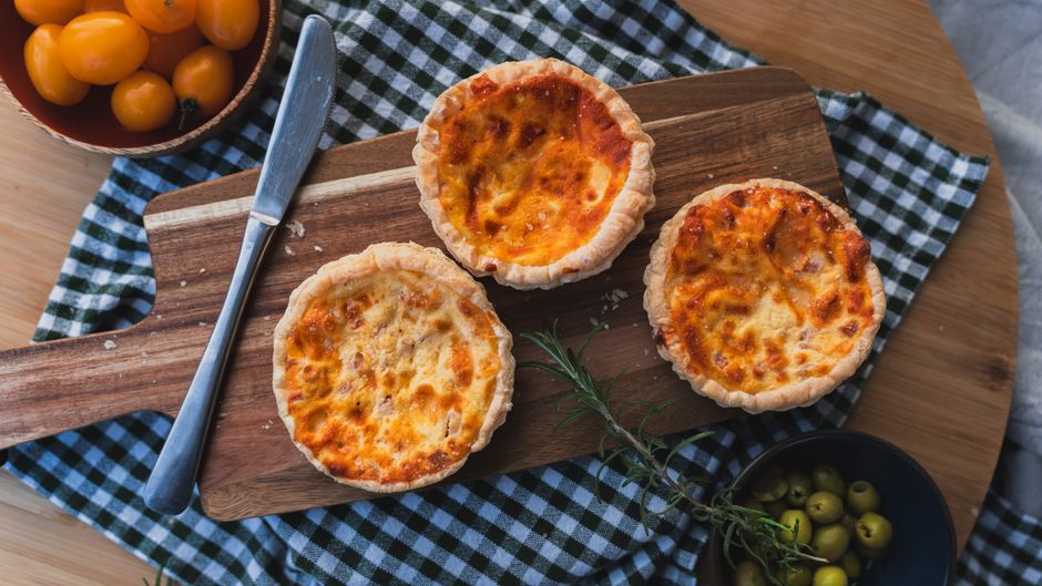 Mini quiches sans pâte sur une planche en bois, garnies de fromage et de légumes, accompagnées d'olive et de tomates cerises.