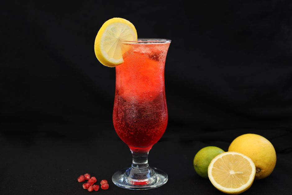 Verre de punch aux fruits rouge décoré d'une rondelle de citron, avec des agrumes en arrière-plan sur fond noir.