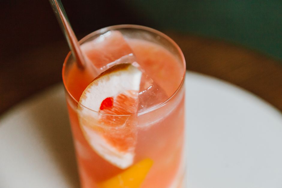 Verre de punch maison aux fruits avec des tranches d'agrumes et des glaçons sur une table en bois.