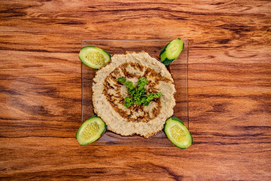 Caviar d'aubergine au four servi dans une assiette avec des tranches de concombre sur un fond en bois.