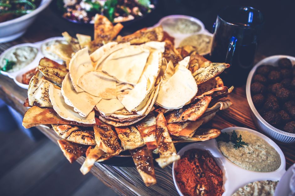 Assiette de pain pita croustillant entourée de divers dips et salades, idéale pour un apéritif convivial.