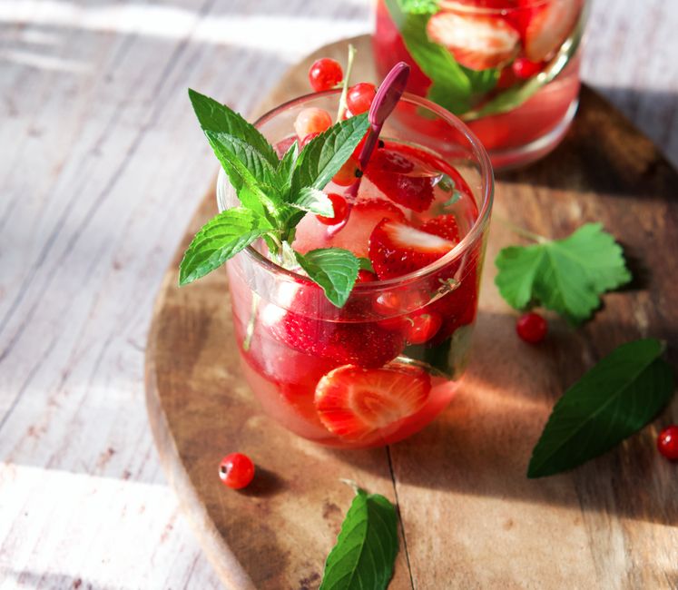 Verres de punch maison aux fruits, garnis de fraises et de menthe, sur une planche en bois. Ambiance festive et légère.